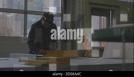 Male carpenter wearing safety goggles marking measurements on wooden plank in workshop, with pencil Stock Photo