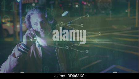 Smiling man wearing bomber jacket holding smartphone to ear on street at night, with binary overlay Stock Photo