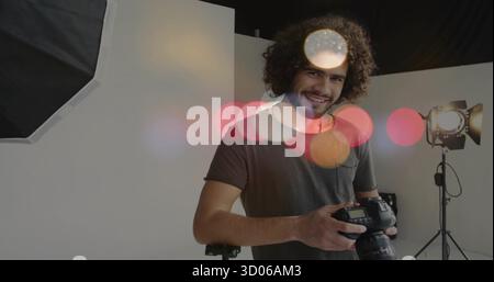 Smiling male photographer holding DSLR camera in studio, with softbox on light stand and strobe Stock Photo