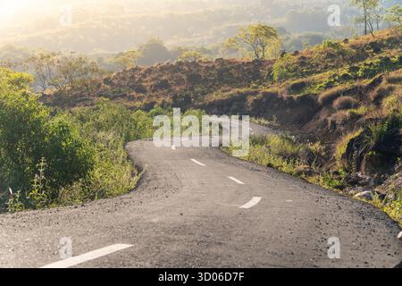 Beautiful low-angle photo of a winding asphalt road through rolling hills at sunrise. Stock Photo