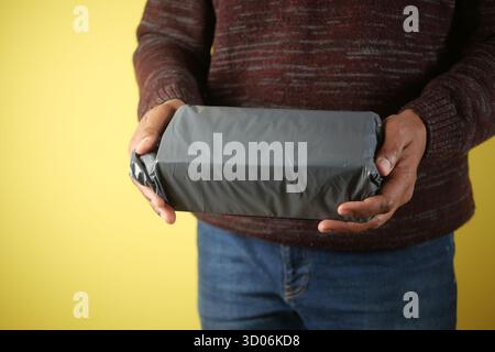 Person holding a wrapped package against a yellow background Stock Photo
