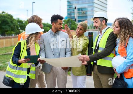 Diverse team of engineers discussing construction blueprint outdoors Stock Photo