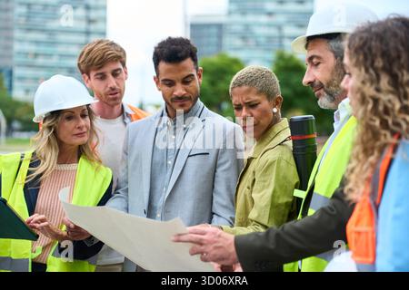 Diverse construction team reviewing blueprint on site Stock Photo