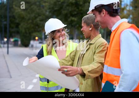 Diverse construction engineers team discussing blueprint outdoors Stock Photo