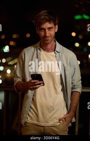 Young man smiling and using smartphone at night Stock Photo