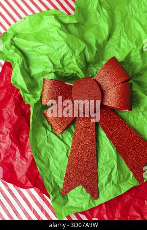 This is a photo of a red glitter bow on a green crumpled tissue paper with a red and white striped background Stock Photo