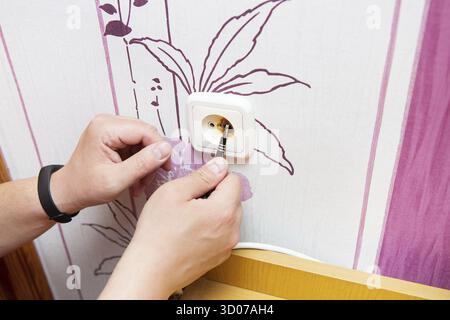The plug and socket are burned, the man is holding a burnt socket.Short circuit, fire, danger. The electrician unscrews the outlet and replaces it Stock Photo