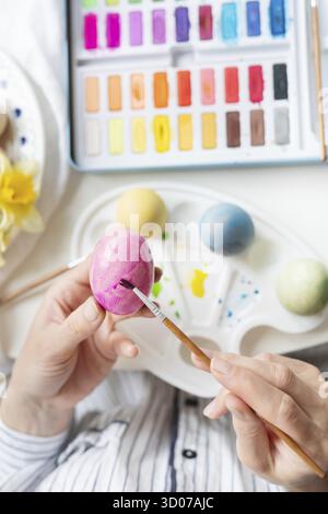 A brush in the process of painting Easter eggs with watercolors. Top view, vertical photo Stock Photo