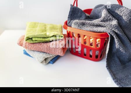 Multi-colored towels lie in a red laundry basket on a white background. Washing and ironing clothes, top view Stock Photo