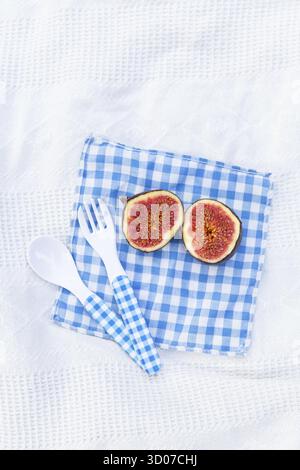 Fresh organic ripe figs cut into two parts lie on a blue checkered napkin. Preparing figs for making jam. Autumn dish. Free space for text Stock Photo