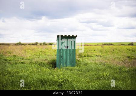 Old green rustic toilet with a heart-shaped hole in the door boards. On open air Stock Photo