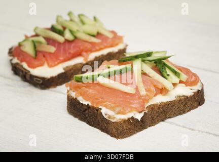 Two open sandwiches with red fish and cucumber on wooden background Stock Photo