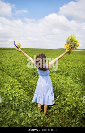 The girl is standing in the field with a bouquet of yellow flowers and a straw hat Stock Photo