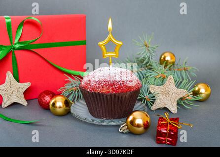 Christmas cupcake with a candle on a gray background. Gift, Christmas tree branches, and decorations. Stock Photo