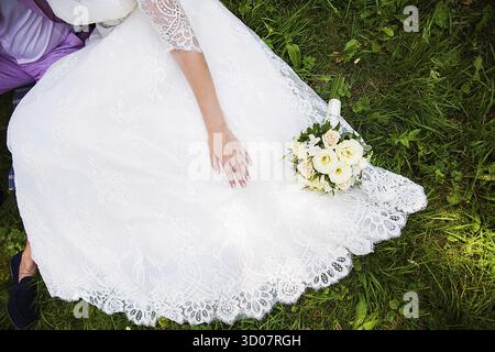 Bride and groom sitting on the grass with beautiful bouquet Stock Photo