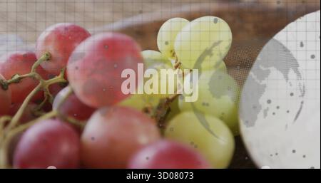 Displaying red and green grapes resting on wooden tabletop, with grid overlay and dotted world map Stock Photo