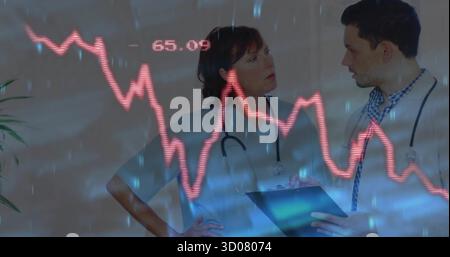 Two doctors wearing white coats examining digital line graphs in medical hallway, with stethoscopes Stock Photo