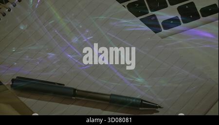 Metallic ballpoint pen resting on spiral notebook on desk by laptop keys, with colored reflections Stock Photo