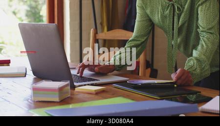Leaning woman in green blouse sorting files on home office table with laptop, copy space Stock Photo