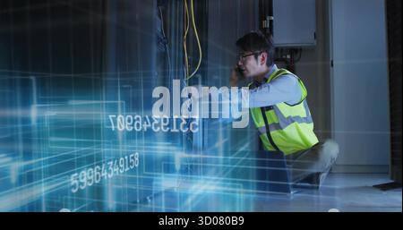 Technician kneeling in server room holding phone adjusting Ethernet cables with overlay, copy space Stock Photo