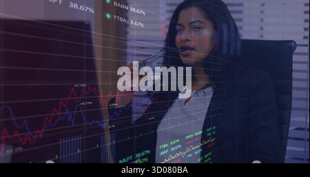 Gazing analyst holding eyeglasses near lips at office desk with stock charts streaming on monitor Stock Photo
