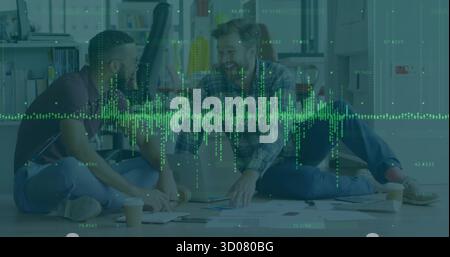 Collaborating men in shirts, jeans working on laptop in office lounge, with papers waveform overlay Stock Photo