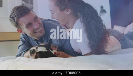Interacting couple lying facing on bed with light bedding in bedroom, including black-and-white dog Stock Photo