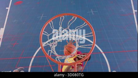 Player wearing yellow red uniform dunking orange basketball in blue court, featuring hoop with net Stock Photo