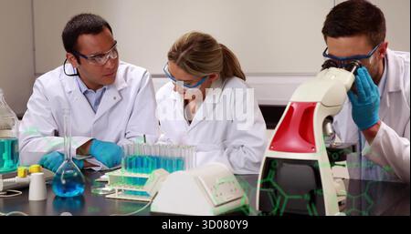 Examining samples scientists in coats and goggles using microscope in lab, with molecular graphics Stock Photo