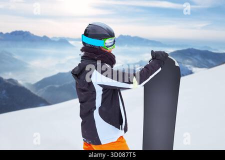 Female snowboarder  standing with snowboard in one hand and enjoying alpine mountain landscape - snowboarding concept Stock Photo