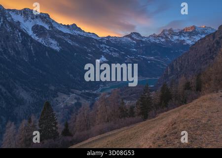 Vivid sunset painting a fiery sky over the mountain range above Poschiavo Valley in Switzerland. Sunset over the snowcapped mountains above the valley Stock Photo