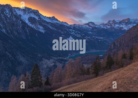 Vivid sunset painting a fiery sky over the mountain range above Poschiavo Valley in Switzerland. Sunset over the snowcapped mountains above the valley Stock Photo