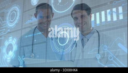 Standing two doctors wearing scrubs, lab coat, stethoscopes viewing digital charts at laptop in lab Stock Photo