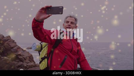 Hiker taking selfie in red jacket on rocky coast, with backpack water bottle smartphone sparkles Stock Photo