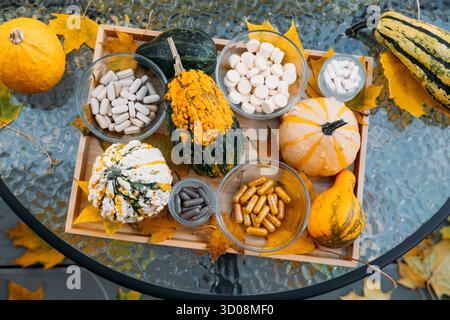 Outdoor tabletop display of autumn gourds and assorted supplements in glass bowls arranged on a wooden tray with fall leaves. Seasonal wellness Stock Photo