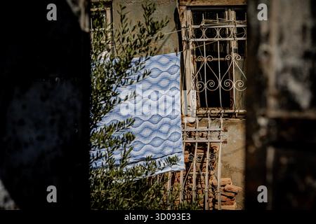Old House With Rusty Window Grate And Blue Patterned Cloth Hanging Outside: Vintage Urban Scene With Weathered Walls And Faded Architecture In Tbilisi Stock Photo