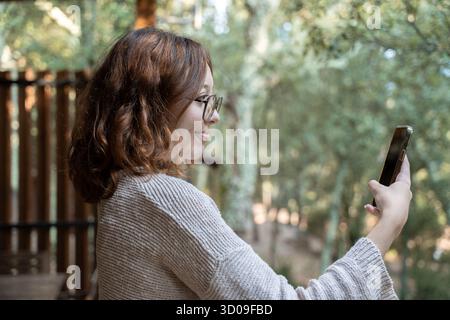 Woman smiling and using smarphone for a video call in a natural outdoor environment Stock Photo