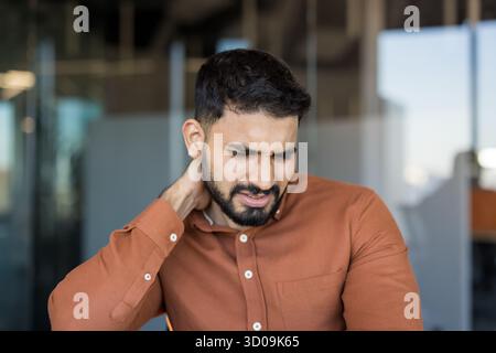 Young man experiencing discomfort and muscle tension in his neck and shoulder due to stress and long working hours, needing relief from chronic pain and discomfort Stock Photo