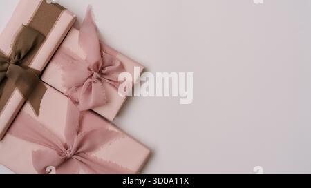 Minimal aesthetic composition with pastel pink gift boxes wrapped in fabric ribbons, placed on a light neutral background. Cozy and elegant flat lay w Stock Photo