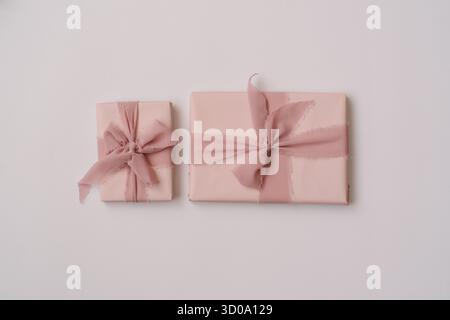 Minimal aesthetic composition with pastel pink gift boxes wrapped in fabric ribbons, placed on a light neutral background. Cozy and elegant flat lay w Stock Photo