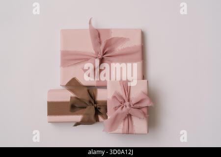 Minimal aesthetic composition with pastel pink gift boxes wrapped in fabric ribbons, placed on a light neutral background. Cozy and elegant flat lay w Stock Photo