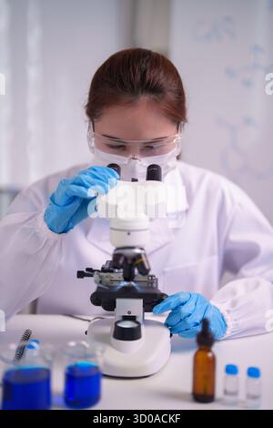 Focused Asian adult woman performing laboratory experiment using microscope discovery work Science research medicine technology development pursuit Stock Photo