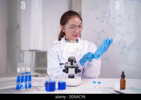 Dedicated Asian scientist prepares for an important chemistry experiment. She wears safety eyewear and protective gloves for lab work. Stock Photo