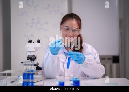 Focused Asian adult woman scientist performs critical chemistry research using a pipette and test tube in a modern lab Stock Photo