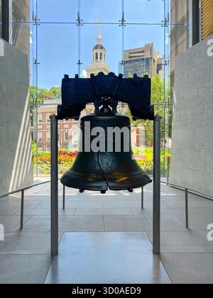 Liberty Bell is on display in a museum. The bell is surrounded by a glass case and is placed in front of a building. The scene is peaceful and serene, Stock Photo