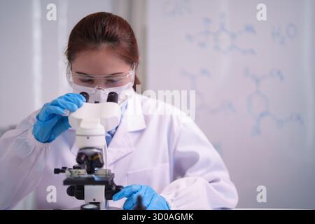 Asian adult scientist meticulously examines samples under microscope in a modern laboratory conducting vital scientific experiments and chemical analy Stock Photo