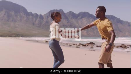 Holding hands couple wearing casual wear leaning back on beach by mountains, wristwatch and rocks Stock Photo