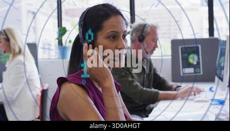 Adjusting headset microphone, woman in purple blouse sitting at white desk with computers in office Stock Photo