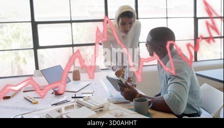 Female architect in beige headscarf and male architect reviewing blueprints in office, with tablet Stock Photo