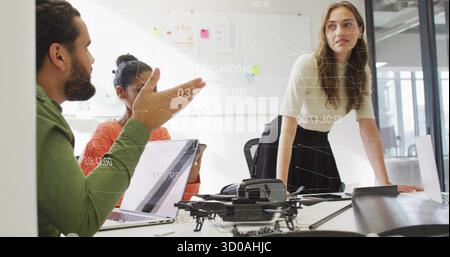 Collaborating team of three discussing plans in modern office, with drone model, laptops and tablet Stock Photo